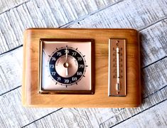 an old fashioned wooden clock sitting on top of a wooden table next to a thermometer