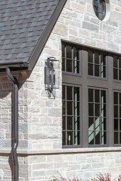 a clock on the side of a brick building with two windows and a weathervane