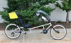 a white bicycle parked on top of a sidewalk next to a tree and shrubbery