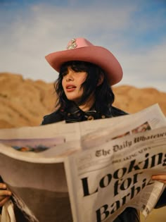 a woman wearing a pink cowboy hat and holding a newspaper