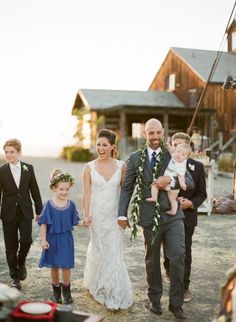 a bride and groom walking with their two children down the aisle in front of an old barn