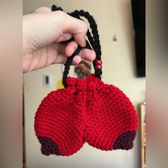 a hand holding a red crocheted bag with black string and two bells attached to it