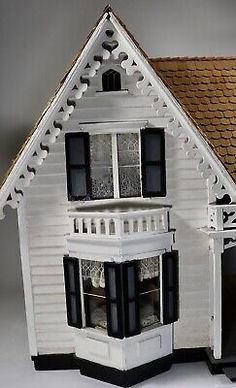 a white doll house with black shutters and brown roof