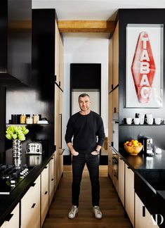 a man standing in the middle of a kitchen with black counter tops and wooden cabinets