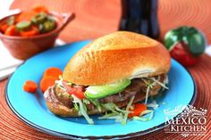 a blue plate topped with a sandwich next to a bowl of veggies and dipping sauce