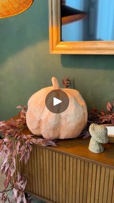 a fake pumpkin sitting on top of a wooden table next to a mirror and potted plant