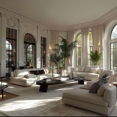 a large living room with white couches and windows on the wall, along with potted palm trees