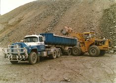 two dump trucks parked next to each other in front of a pile of dirt and rocks