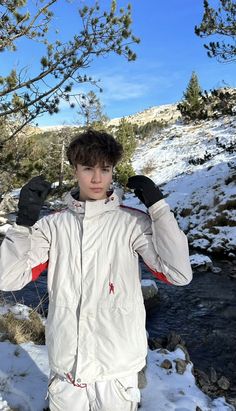 a young man standing in the snow next to a tree