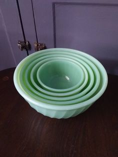 a stack of green bowls sitting on top of a wooden table next to a purple door