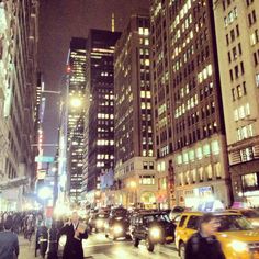 a busy city street at night with cars and people walking on the sidewalk in front of tall buildings