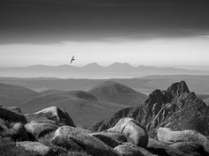 black and white photograph of mountains with birds flying over them in the distance, taken from high above