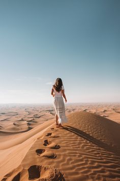 a woman in white dress walking across sand dunes