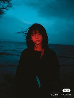 a woman standing on top of a beach next to the ocean under a cloudy sky