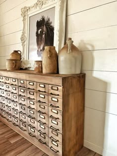 a wooden cabinet with vases on top of it in front of a horse painting