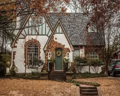 a white brick house with green trim and arched windows in the front yard surrounded by autumn leaves