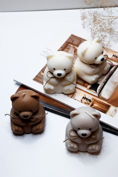 three small teddy bears sitting on top of a table next to an open notebook and pen