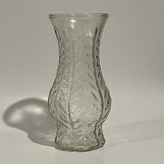 a clear glass vase sitting on top of a white tablecloth covered floor next to a wall