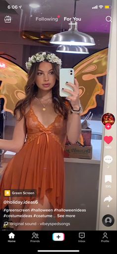 a woman in an orange dress taking a selfie with her cell phone and butterfly wings