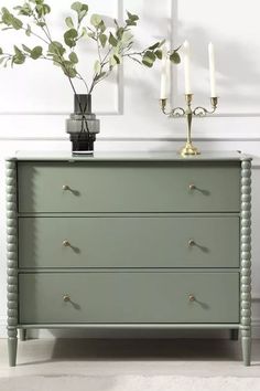 a green chest of drawers with candles on top and a potted plant next to it