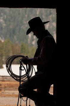 a man sitting on top of a horse next to a roped in area with mountains in the background