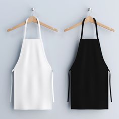 two black and white aprons hanging on wooden hangers next to each other,