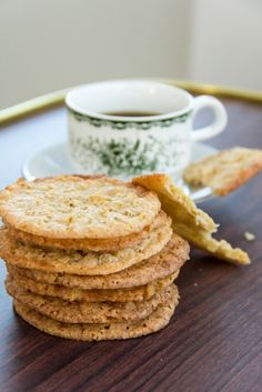 a stack of crackers next to a cup of tea on a wooden table with a saucer