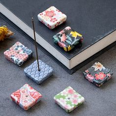 there are many small pieces of fabric sitting on the floor next to a book and some flowers