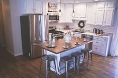 a kitchen with white cabinets and stainless steel appliances is pictured in this image, there are four stools at the center of the island