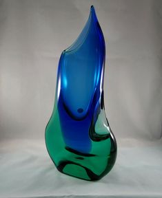 a blue and green glass vase sitting on top of a white table next to a wall