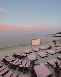 an empty beach with many tables and chairs covered in pink blankets on the sand at sunset