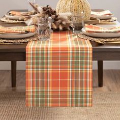 an orange plaid table runner on top of a wooden table with place settings and utensils