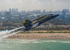 a blue and yellow fighter jet flying over the ocean next to a cityscape