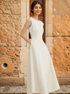 a woman standing in front of a stone building wearing a white dress