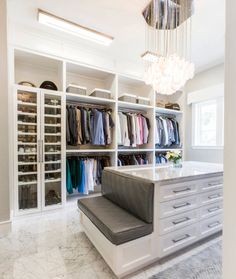 a walk in closet filled with lots of clothes and drawers next to a chandelier