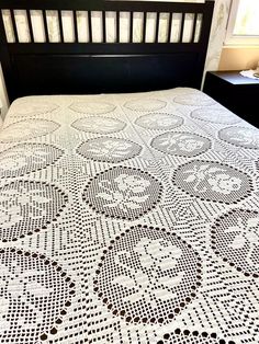 a crocheted bedspread on a bed with a black wooden headboard