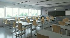 an empty classroom with desks and chalkboards on the wall in front of large windows