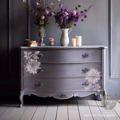 two vases with flowers sit on top of an old chest of drawers in a room