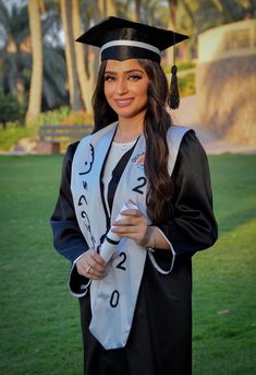 a woman wearing a graduation cap and gown standing in the grass with her hand on her hip