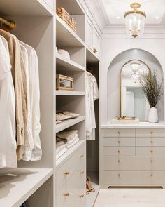 a walk - in closet with white cabinets and drawers, gold handles on the doors