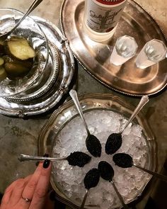 a person is holding two spoons in front of an ice bucket with pickles on it