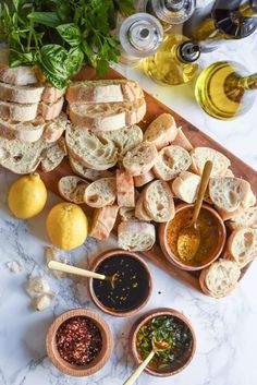 an assortment of breads and dipping sauces on a cutting board with lemons