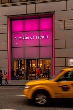 a yellow taxi driving past a victoria's secret store