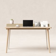 a laptop computer sitting on top of a wooden table next to a cup and plant