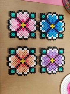 four cross stitch coasters on a table next to a plate with a pink and blue flower