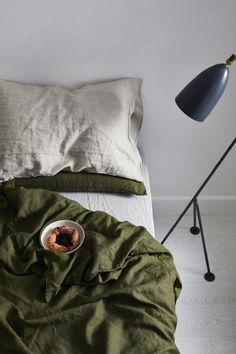 a bed with a green comforter next to a black lamp and a white pillow