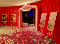 a room with red drapes and paintings on the floor, lit up by lights