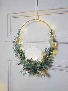 a wreath hanging on the front door with lights around it and a house in the background