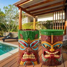 two tiki masks sitting on top of a wooden deck next to a pool