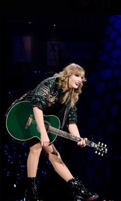 taylor swift performing on stage with her green guitar in hand and smiling at the camera